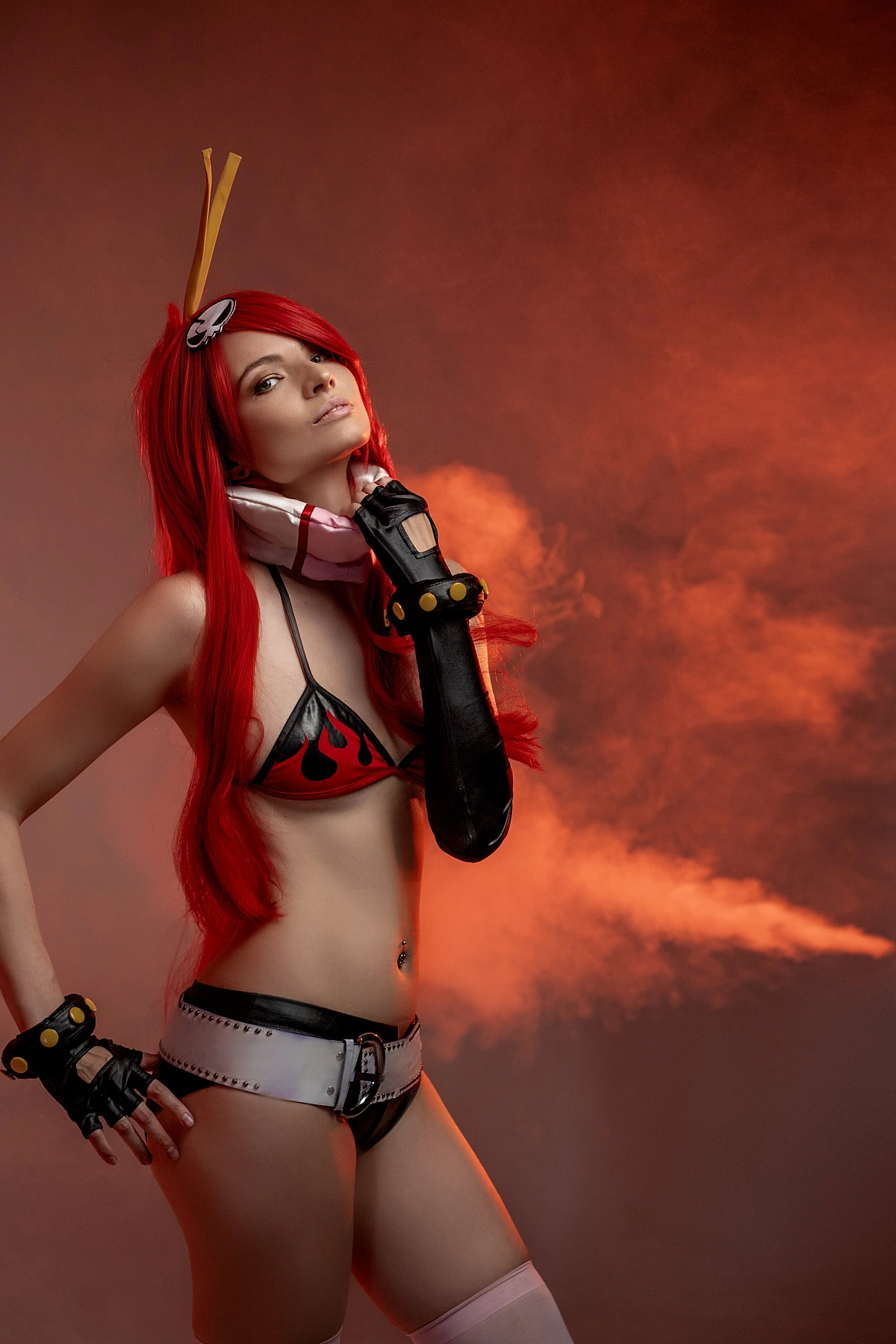 Red-haired cosplay model in flame bikini, gloves and belt, posing in smoky red studio lighting
