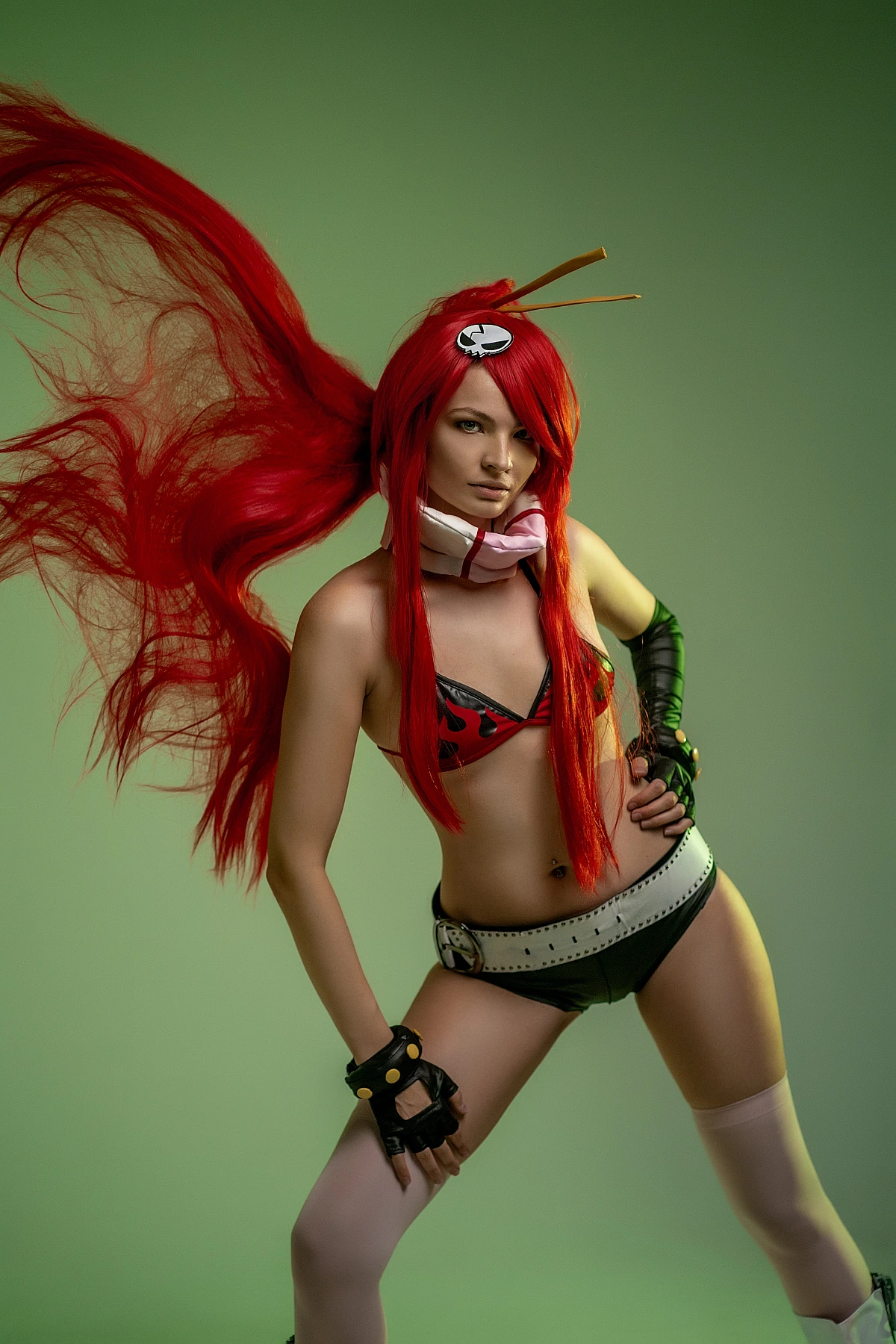 Cosplay model with flowing red hair in flame bikini pose against green studio background