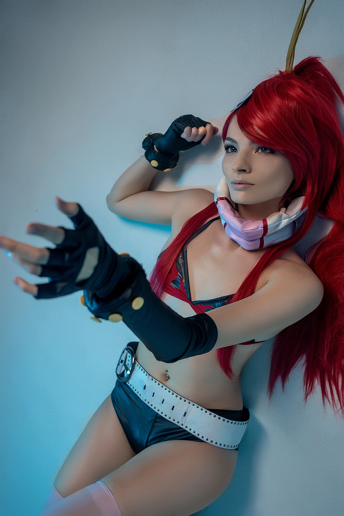 Red-haired cosplay model leaning against wall in flame bikini with gloves under blue light